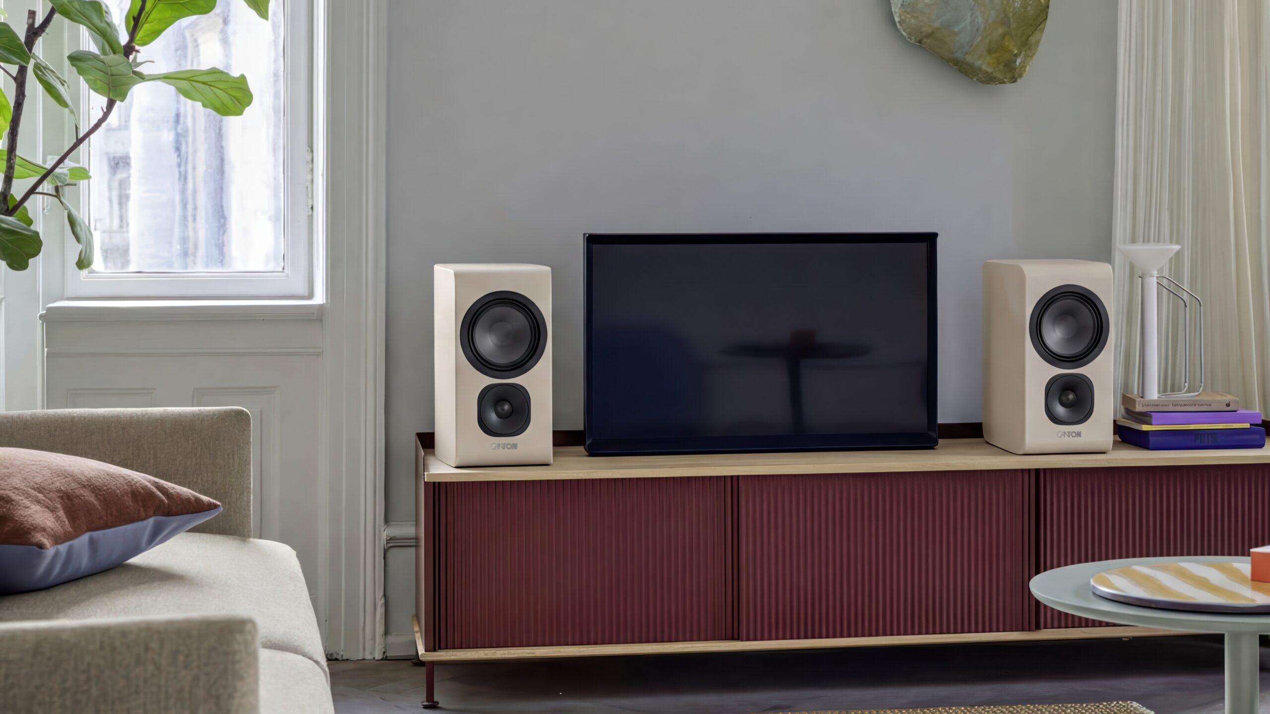 Canton Vento 2026: Ni modeller fra stereo til Atmos 5 To kremfargede Canton Vento hyllehøyttalere står på en rødfarget sideboard sammen med en TV i et lyst stuemiljø med et grønt tre i bakgrunnen.Bildetekst: For mindre rom holder det med hyllemodellene Vento 21 eller 31, som har bakvendt bassrefleks og dermed er enklere å plassere tett mot vegg.