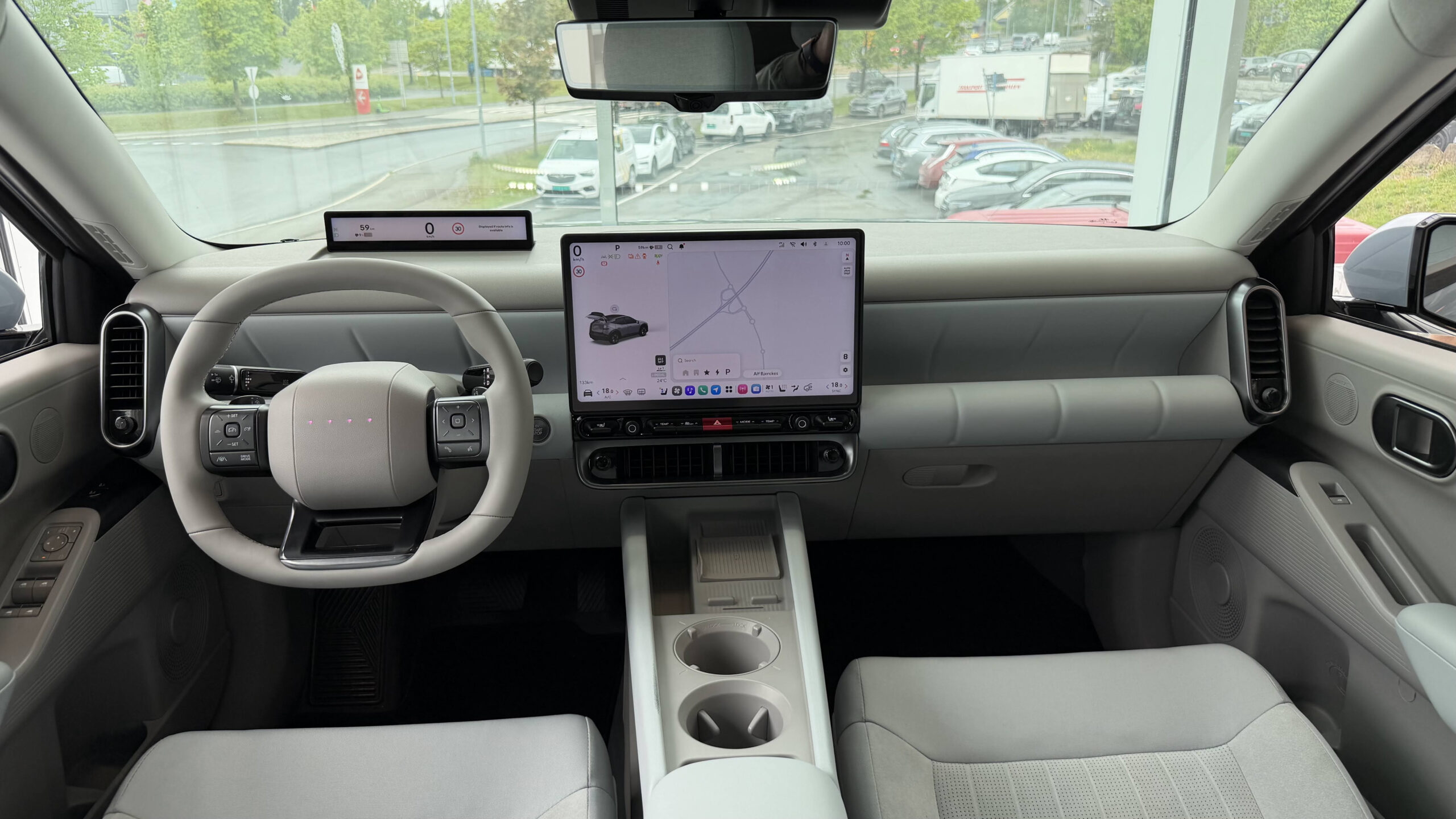 Ioniq 3: Urban elbil med smart teknologi 2 Interiør i Hyundai Ioniq 3 med lyst grått stoff, stor liggende midtskjerm, smal fargeskjerm bak rattet og midtkonsoll med koppholdere.
