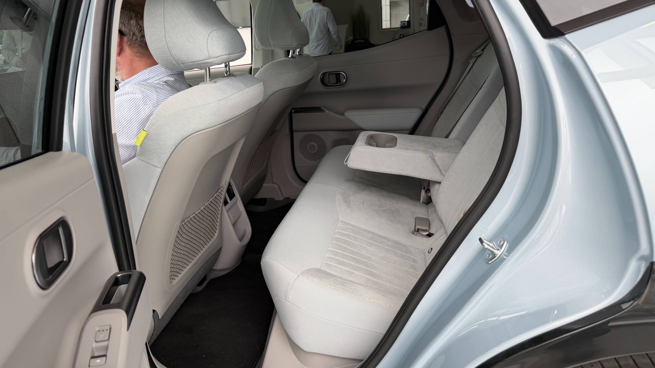 Ioniq 3: Urban elbil med smart teknologi 4 Baksete i Hyundai Ioniq 3 i lyst grått stoff, med nedfelt midtarmlene og koppholdere, sett gjennom åpen bakdør.
