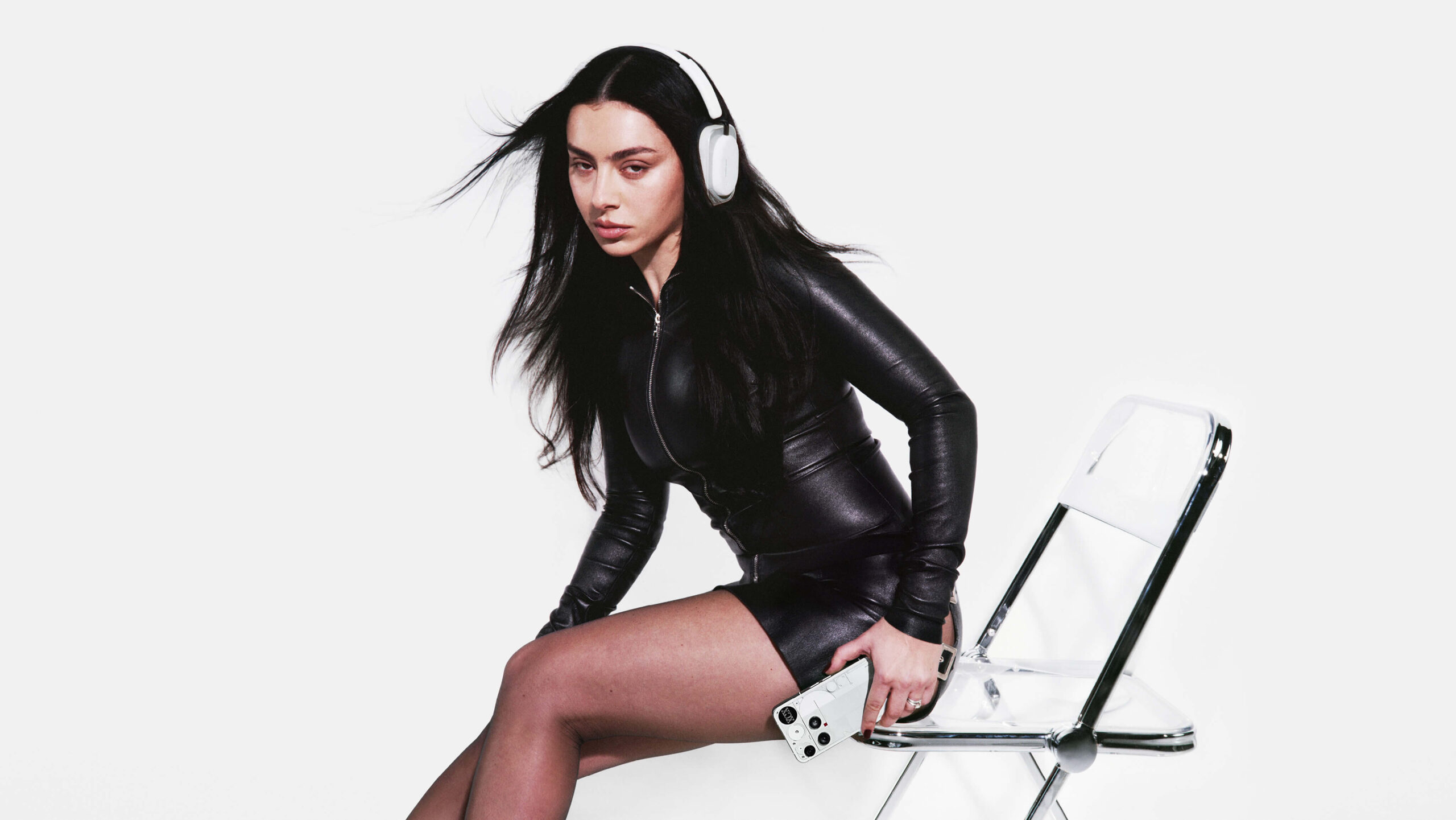 Nothing Headphone (a) 1 Kvinne med hvite Nothing Headphone (a) lent mot en gjennomsiktig akrylstol