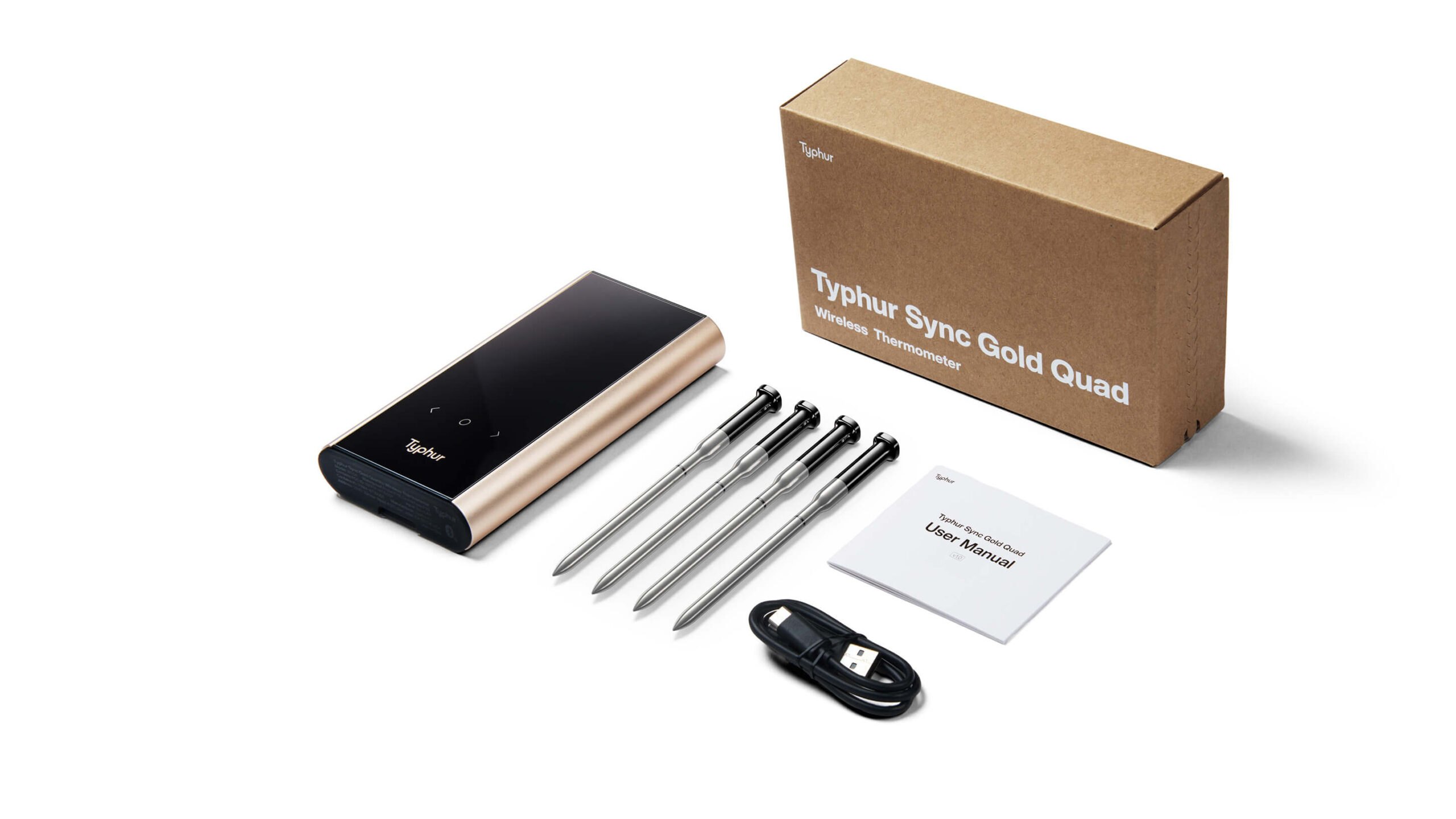 Typhur Sync Gold steketermometer: Alle får biffen som de vil 1 Innholdet i Typhur Sync Gold Quad-esken oppstilt på hvit bakgrunn: basestasjon i sort med champagnefarget aluminiumsside, fire metallsonder på rekke, brun produkteske merket "Typhur Sync Gold Quad Wireless Thermometer", brukermanual og en USB-kabel.