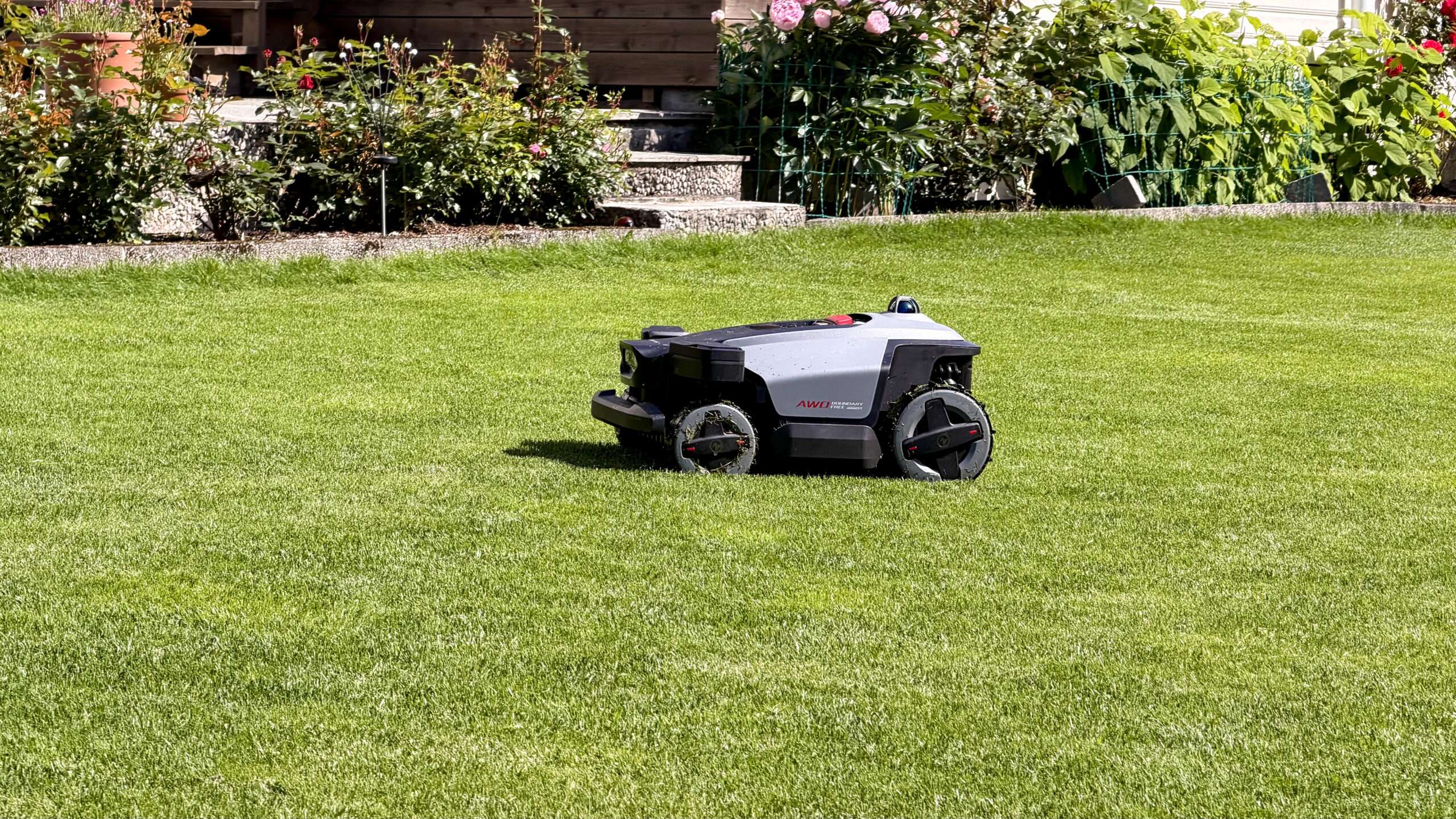 Roborock RockMow Z120 LiDAR 8 Roborock RockMow Z120 LiDAR står på en nyklippet plen foran et fargerikt blomsterbed.