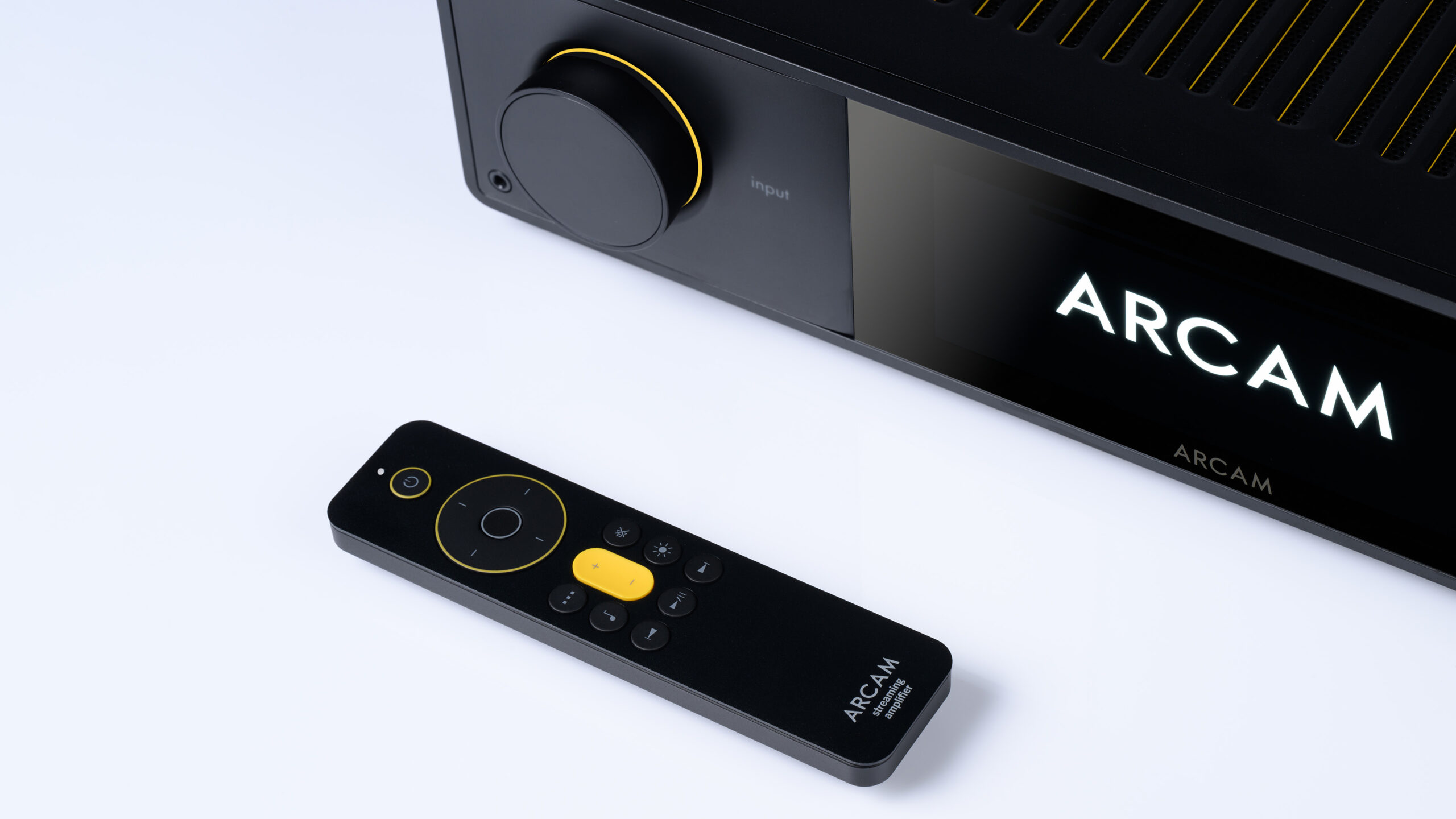 Arcam SA35 1 Nærbilde av fronten på Arcam SA35 med opplyst logo, med den medfølgende fjernkontrollen liggende foran.