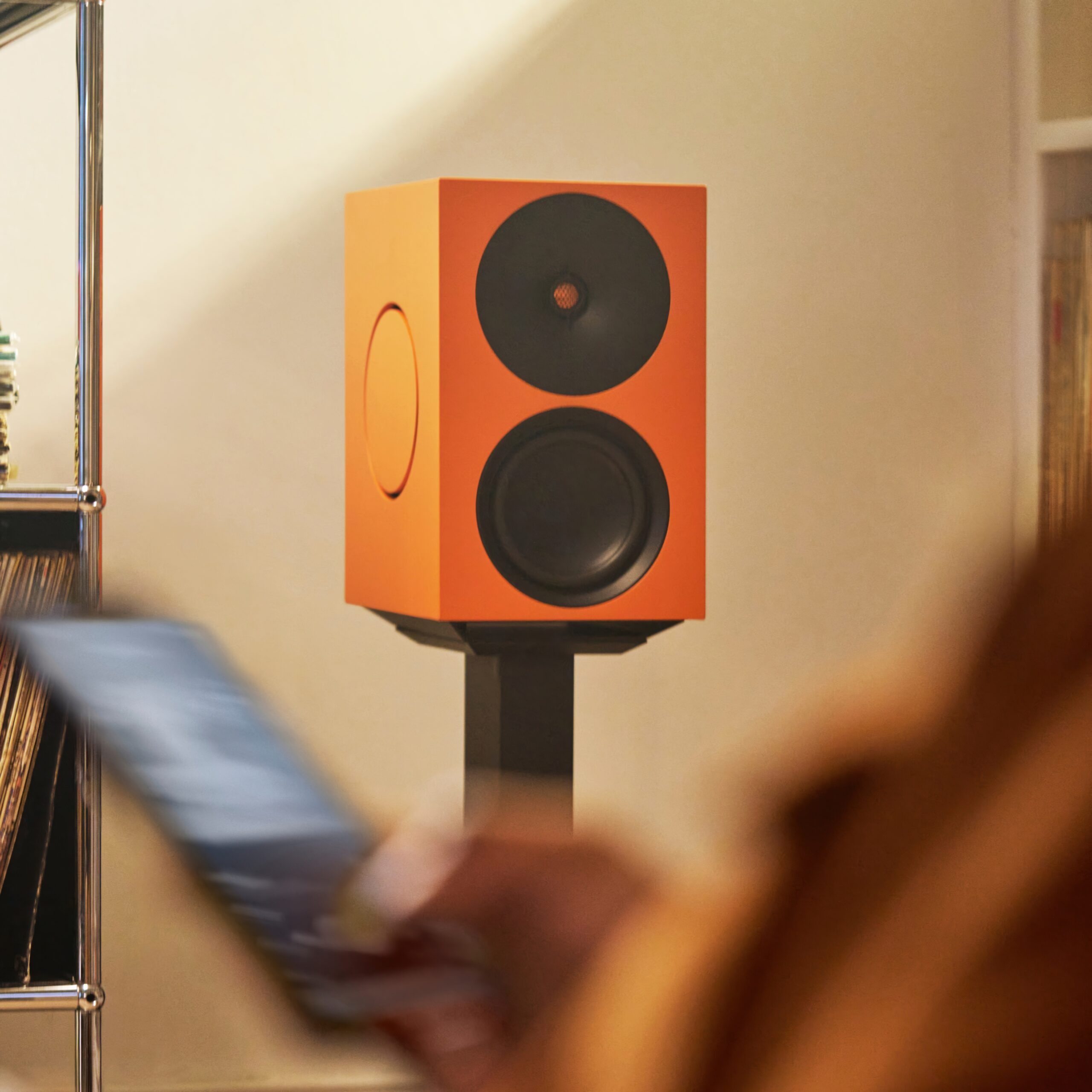 Cambridge Audio L/R X 4 Cambridge Audio L/R X i oransje på stativ mens en person betjener den fra mobilen.